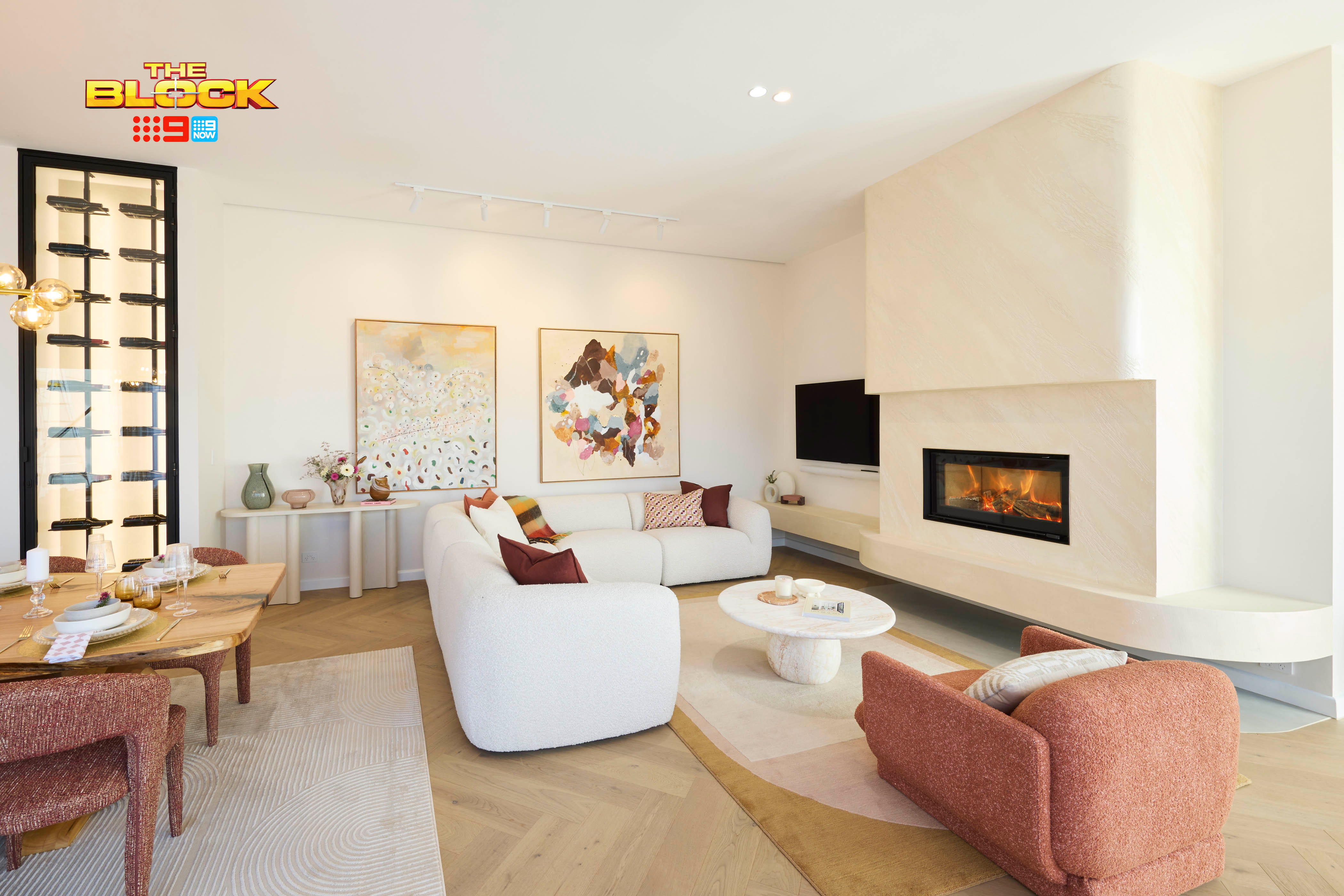 Modern gas fireplace with realistic burning logs set in a light-coloured wall next to a wooden side table with books.