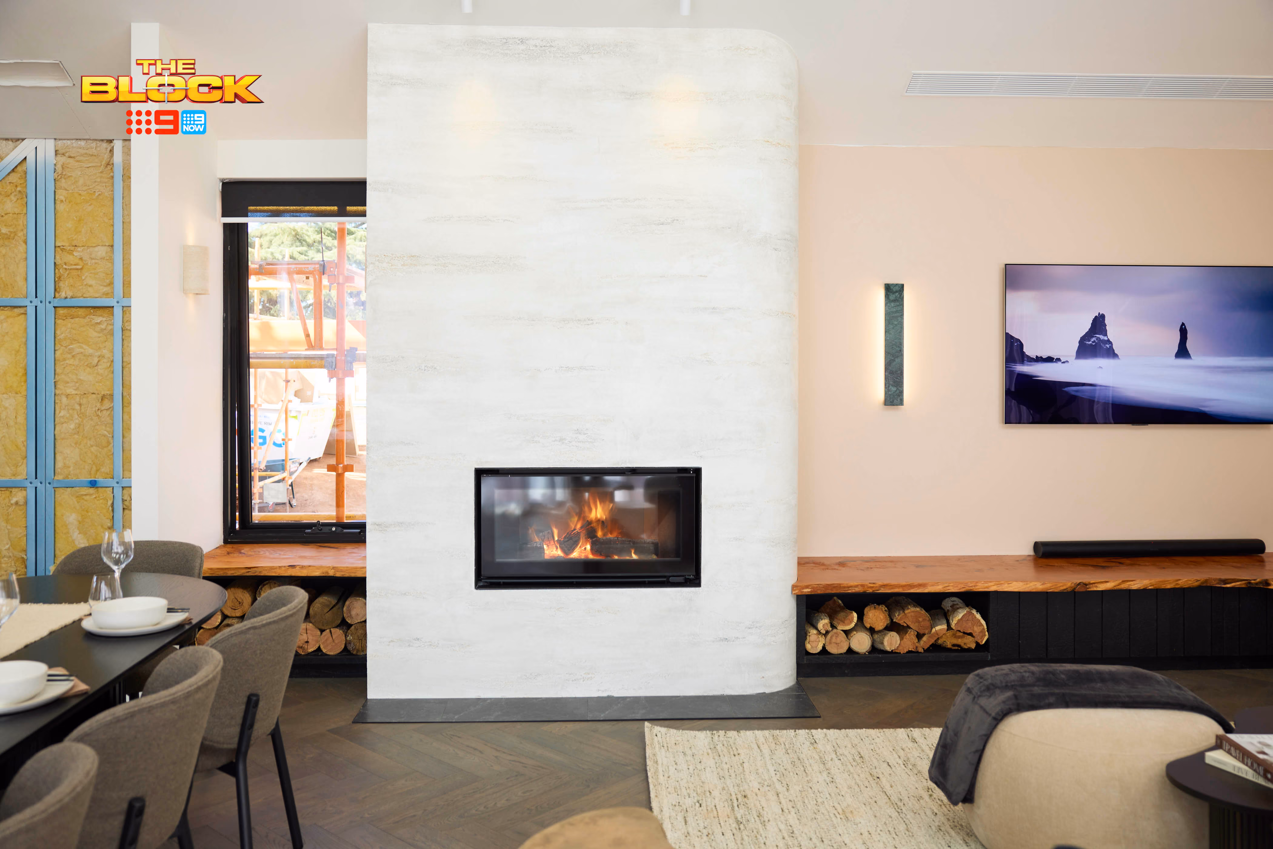 Modern gas fireplace with realistic burning logs set in a light-coloured wall next to a wooden side table with books.