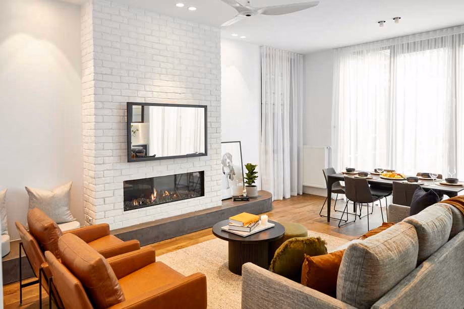 Modern gas fireplace with realistic burning logs set in a light-coloured wall next to a wooden side table with books.