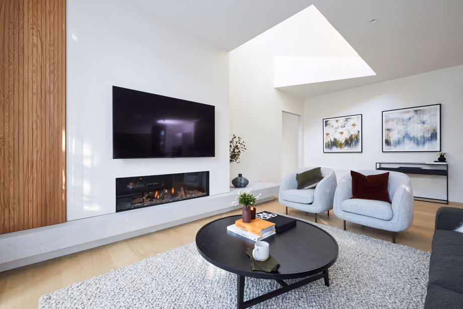 Modern gas fireplace with realistic burning logs set in a light-coloured wall next to a wooden side table with books.