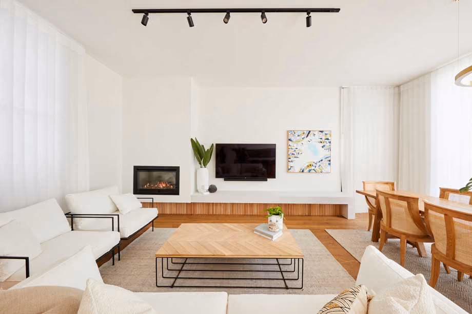 Modern gas fireplace with realistic burning logs set in a light-coloured wall next to a wooden side table with books.
