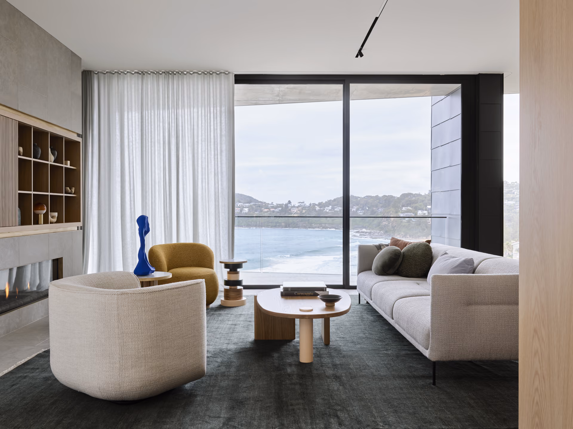 Modern gas fireplace with realistic burning logs set in a light-coloured wall next to a wooden side table with books.