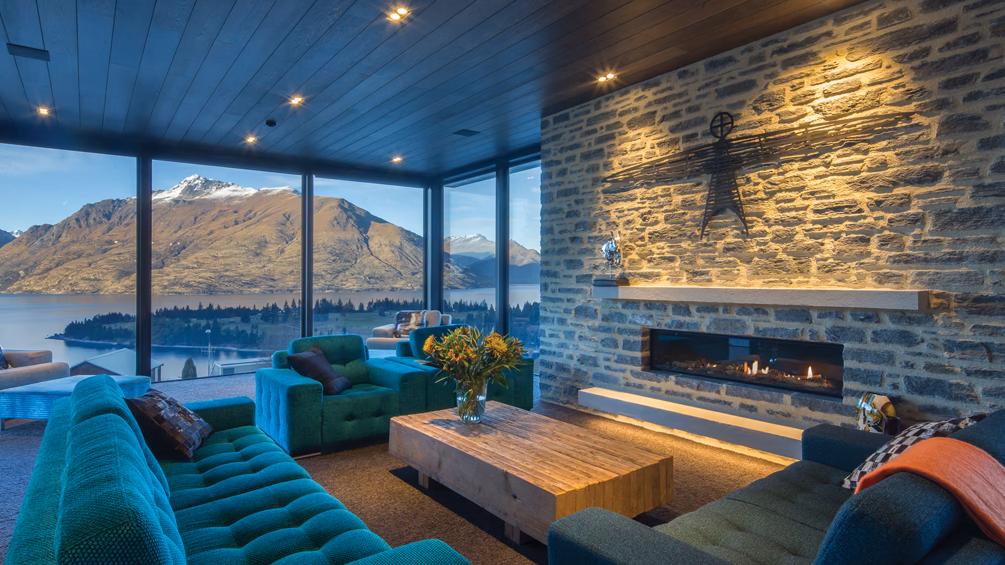 Modern gas fireplace with realistic burning logs set in a light-coloured wall next to a wooden side table with books.