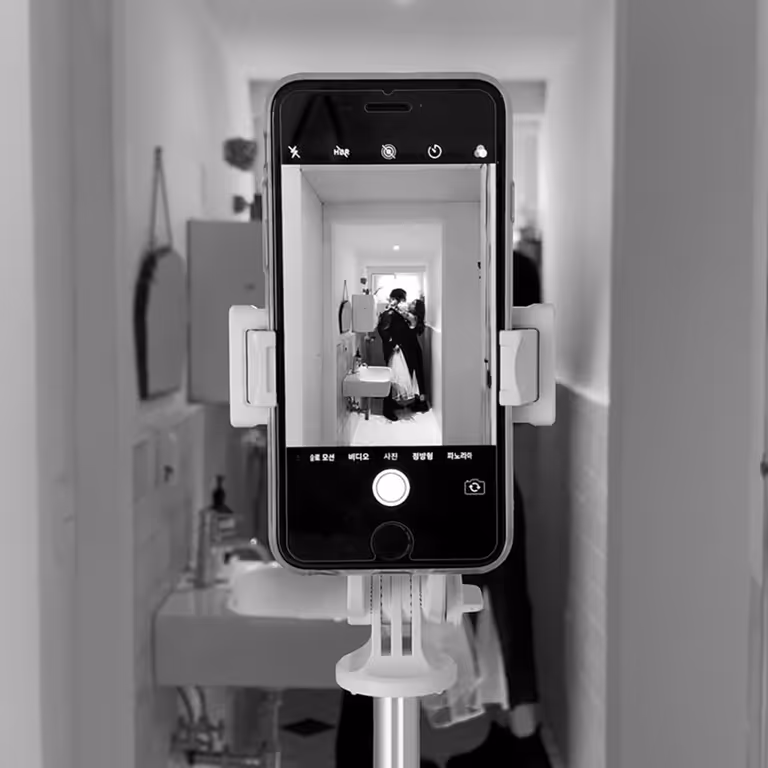 Un smartphone fixé sur un trépied filme un couple s'embrassant dans un petit couloir.