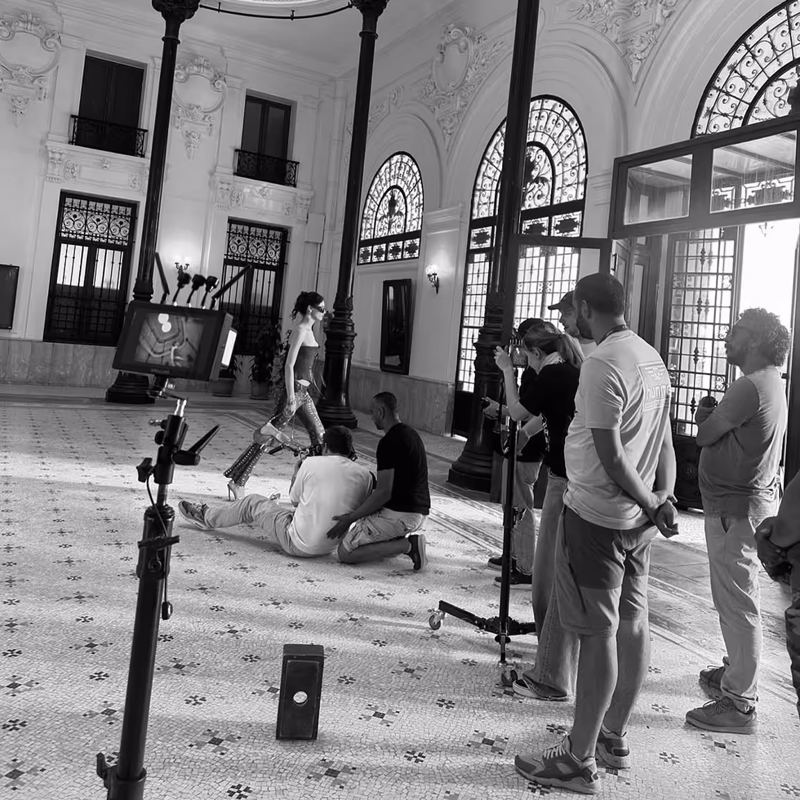 Une équipe de tournage filme un mannequin marchant dans un intérieur avec de grandes fenêtres et colonnes décoratives.