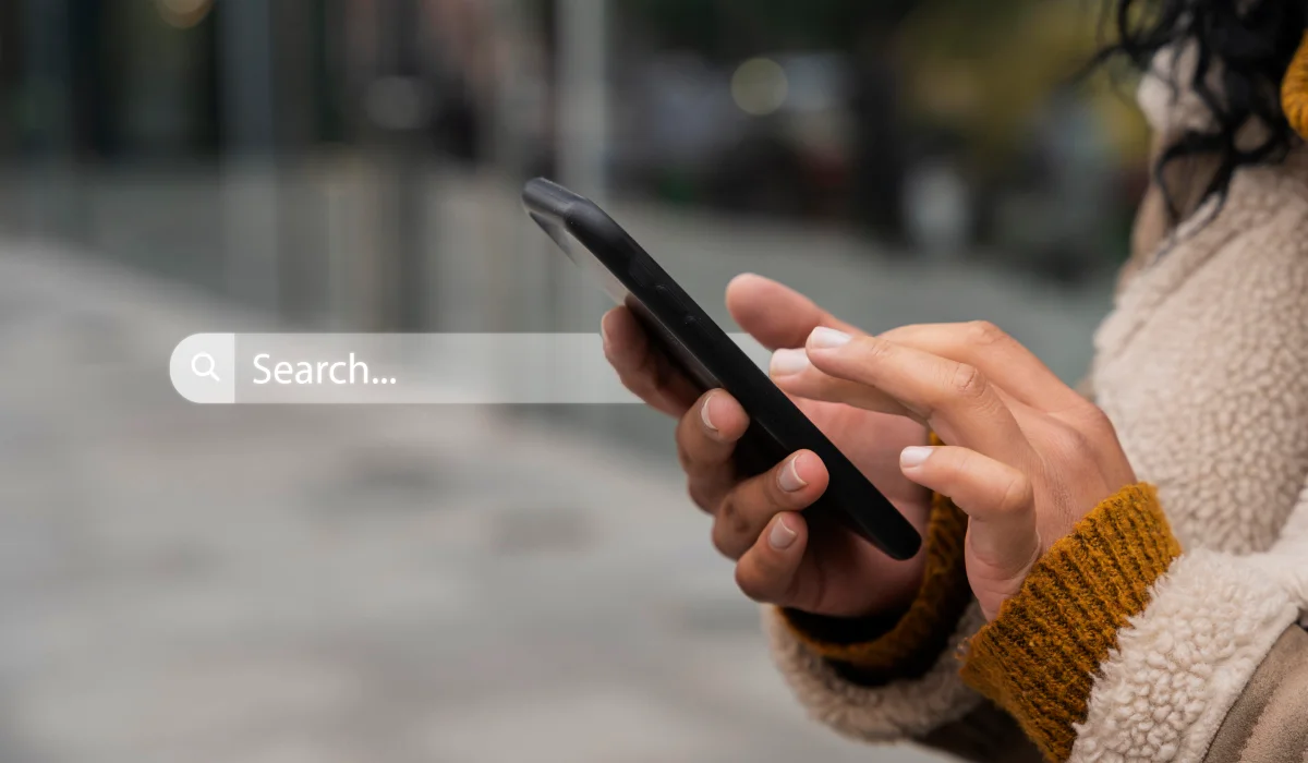 Person using a smartphone outdoors with a search bar overlay showing the word 'Search...'.
