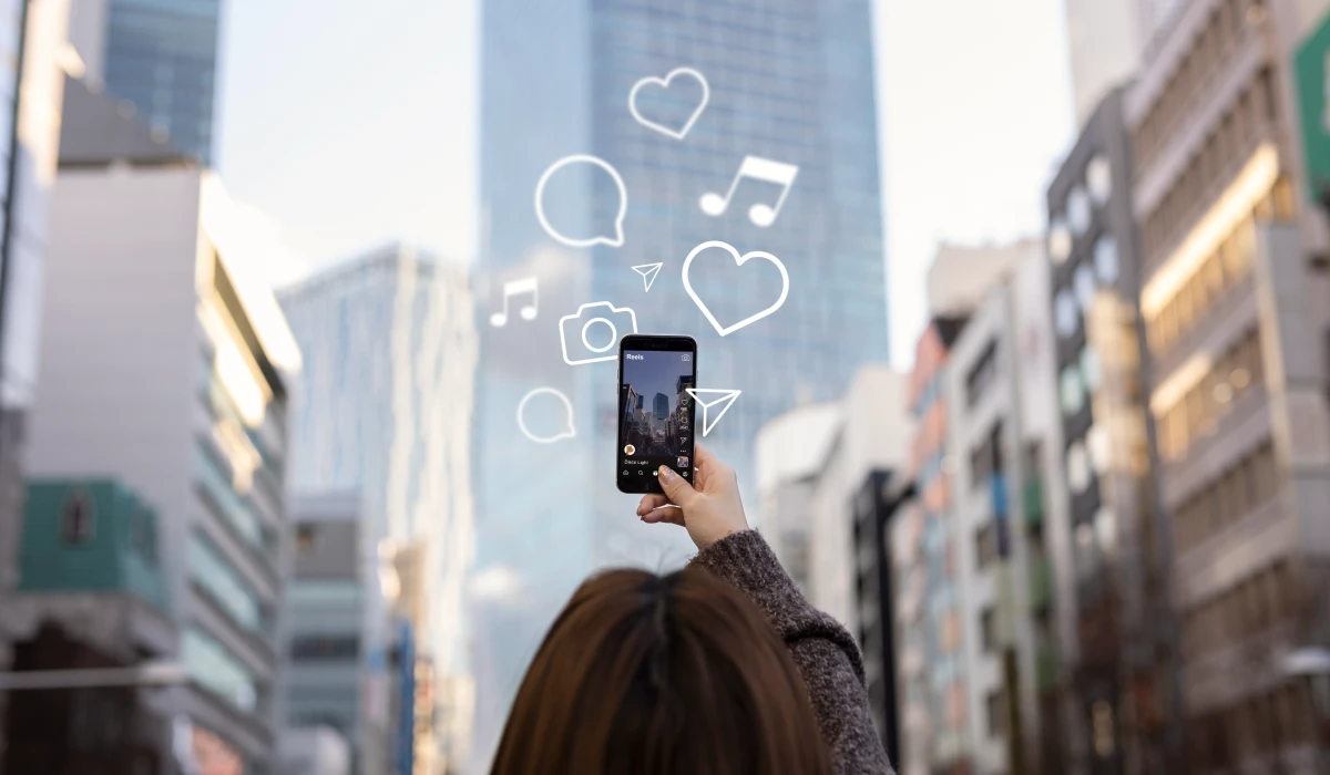 Person holding up smartphone to record video in urban setting with social media icons overlay.