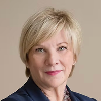 Portrait of a middle-aged woman with short blonde hair wearing a navy blazer against a beige background.