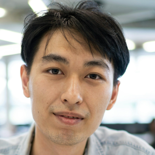 Close-up portrait of a young man with dark hair and a slight smile in a softly lit indoor setting.