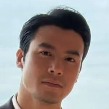 Close-up portrait of a man with short black hair against a light background.