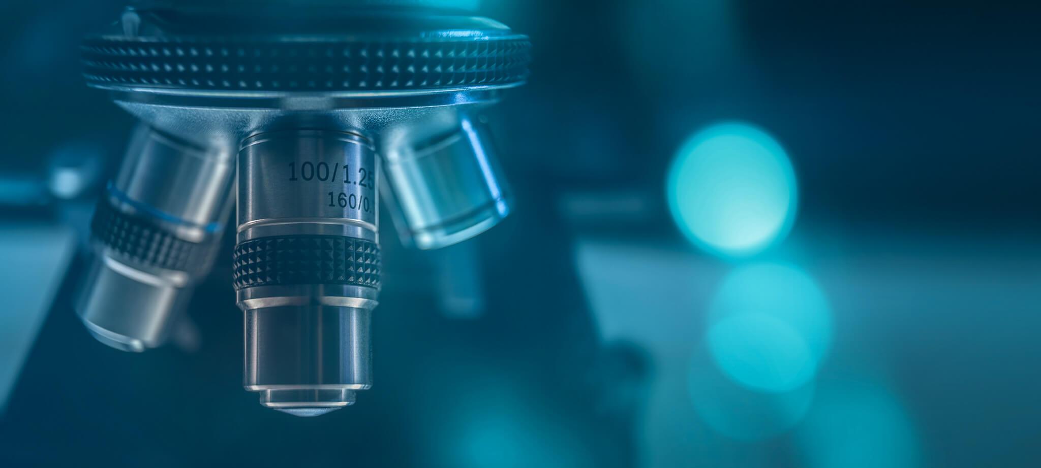 Close-up of microscope objective lenses with blue bokeh background.