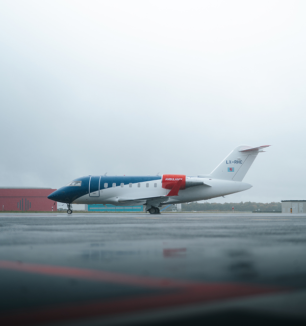 Medical ambulance jet aircraft parked on a wet runway with overcast sky.