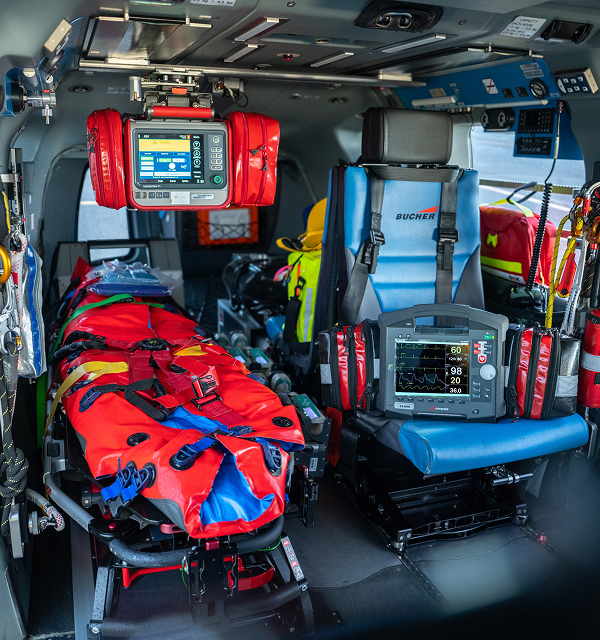 Interior of a medical helicopter equipped with a stretcher covered in red and blue straps, medical monitors, and emergency equipment.