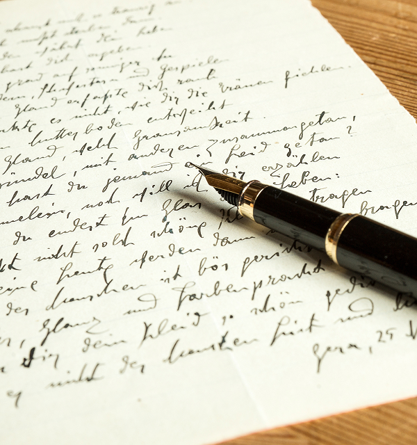 Close-up of a black fountain pen resting on a handwritten letter with cursive script on white paper.