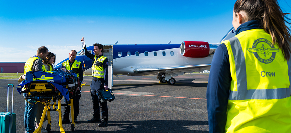 Medical crew preparing a patient on a stretcher near an ambulance airplane on a tarmac under clear blue sky.