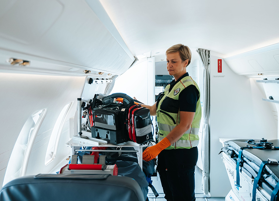 Female emergency responder wearing a safety vest and gloves organizing medical equipment inside an aircraft.