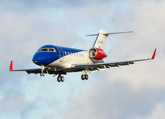 Blue and white private jet airplane with red engine accents flying against a cloudy sky.