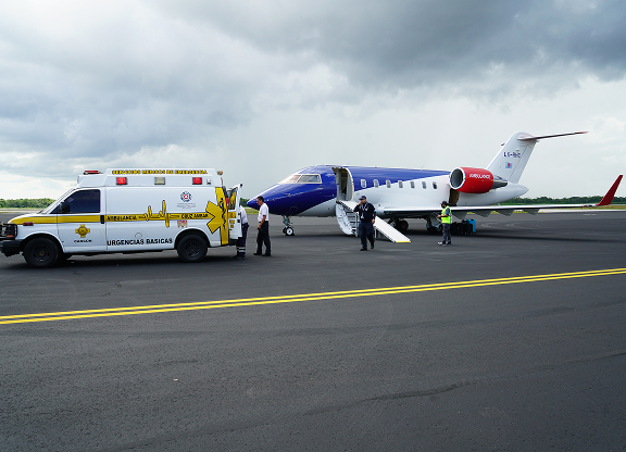 Ambulance and medical personnel next to a private jet on an airport tarmac under a cloudy sky.