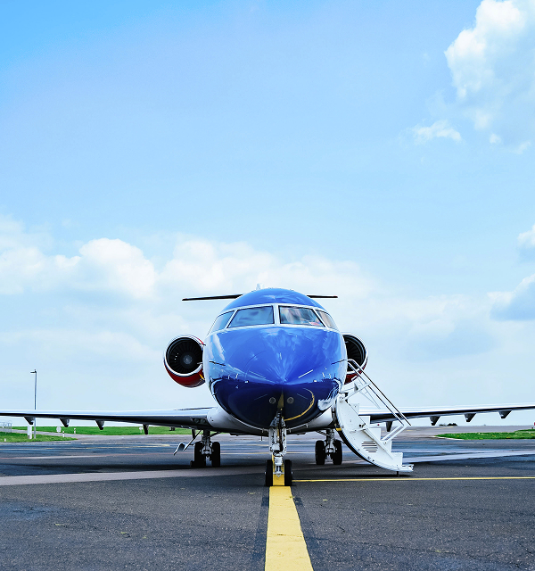 Front view of a blue and white private jet on the runway with stairs extended under a partly cloudy sky.