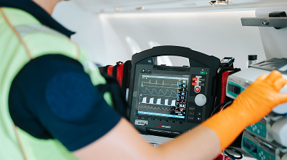 Medical professional operating a portable defibrillator with vital signs displayed on the screen.