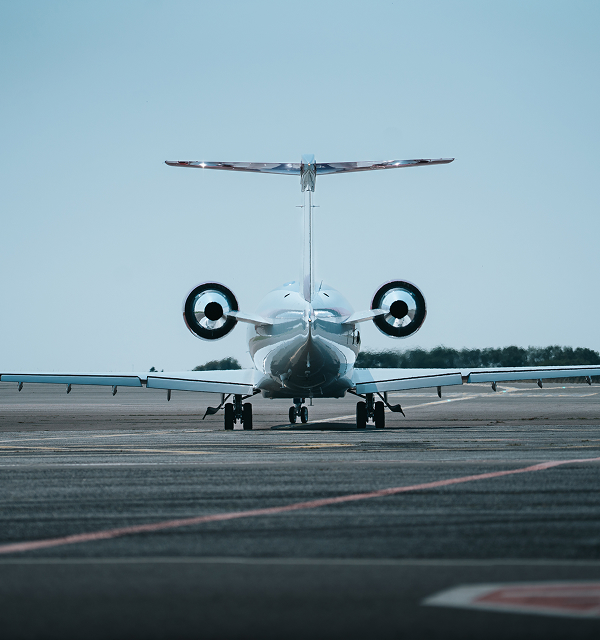 Rear view of a private jet on an airport runway under clear sky.