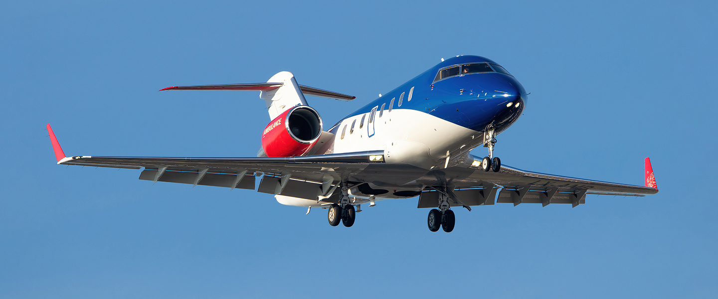 Blue, white, and red airplane approaching for landing against a clear blue sky.