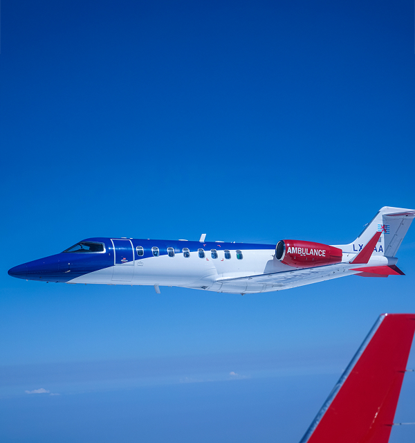 Side view of a white and blue Learjet ambulance flying against a clear blue sky.