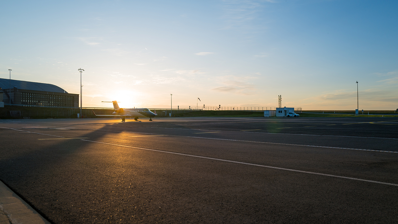 Small private jet parked on an airport tarmac at sunset with a clear sky.