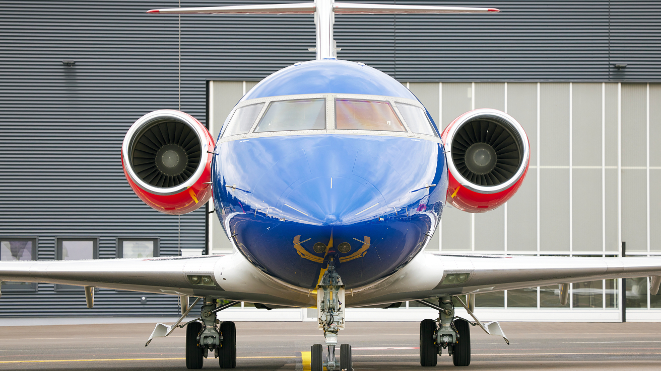 Front view of a blue and white private jet with red engine intakes parked on a runway in front of a building.