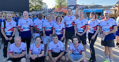 Group of runners wearing matching white and blue shirts posing together outdoors before a race.