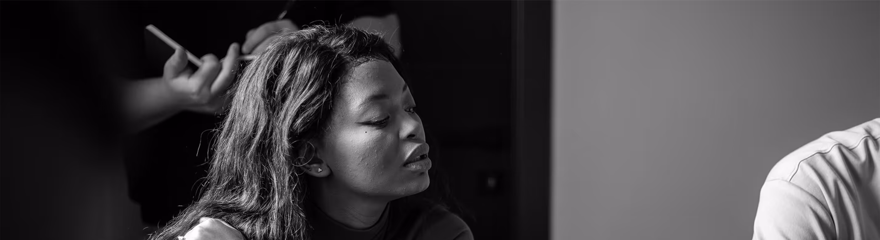 Black and white image of a woman getting her hair styled by a person holding a brush.