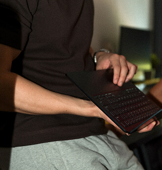Hands holding a compact orange camera with a black circular lens and an adjustable handle.