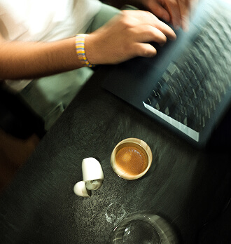 Hands holding a compact orange camera with a black circular lens and an adjustable handle.