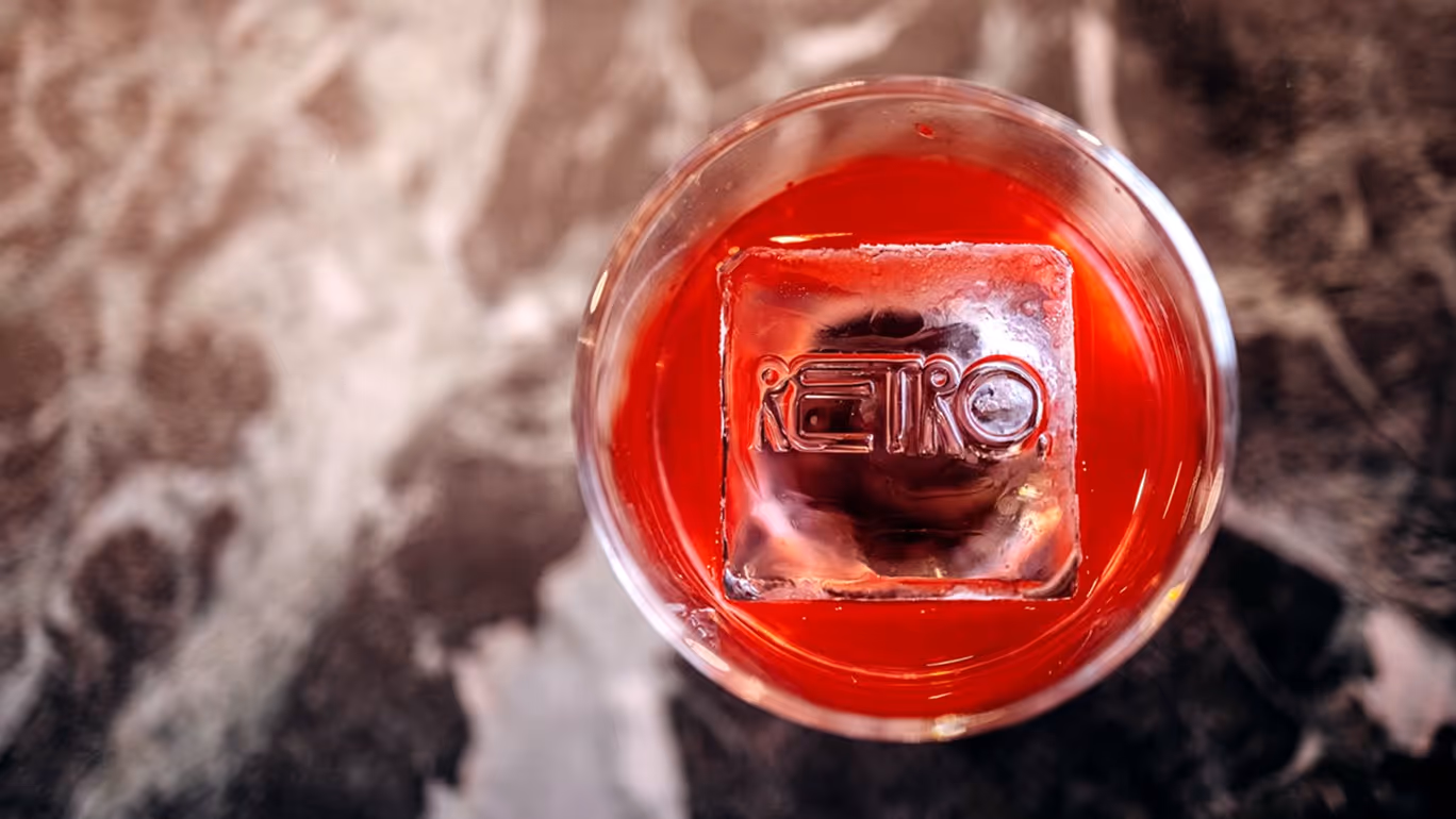 Top view of a red drink with a large ice cube engraved with the word RETRO.