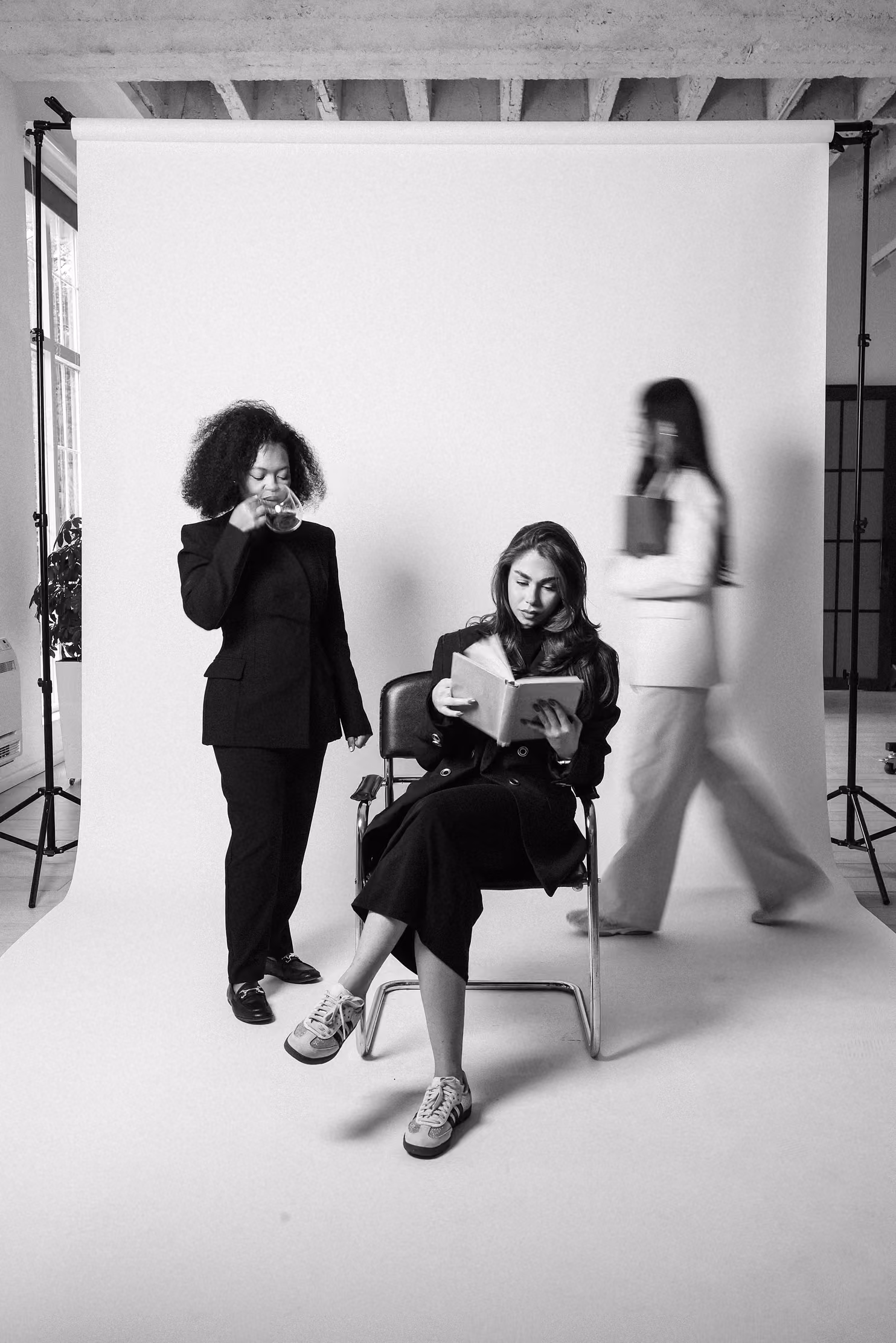 One women walking, other drinking coffee, third sitting on chair and reading a book