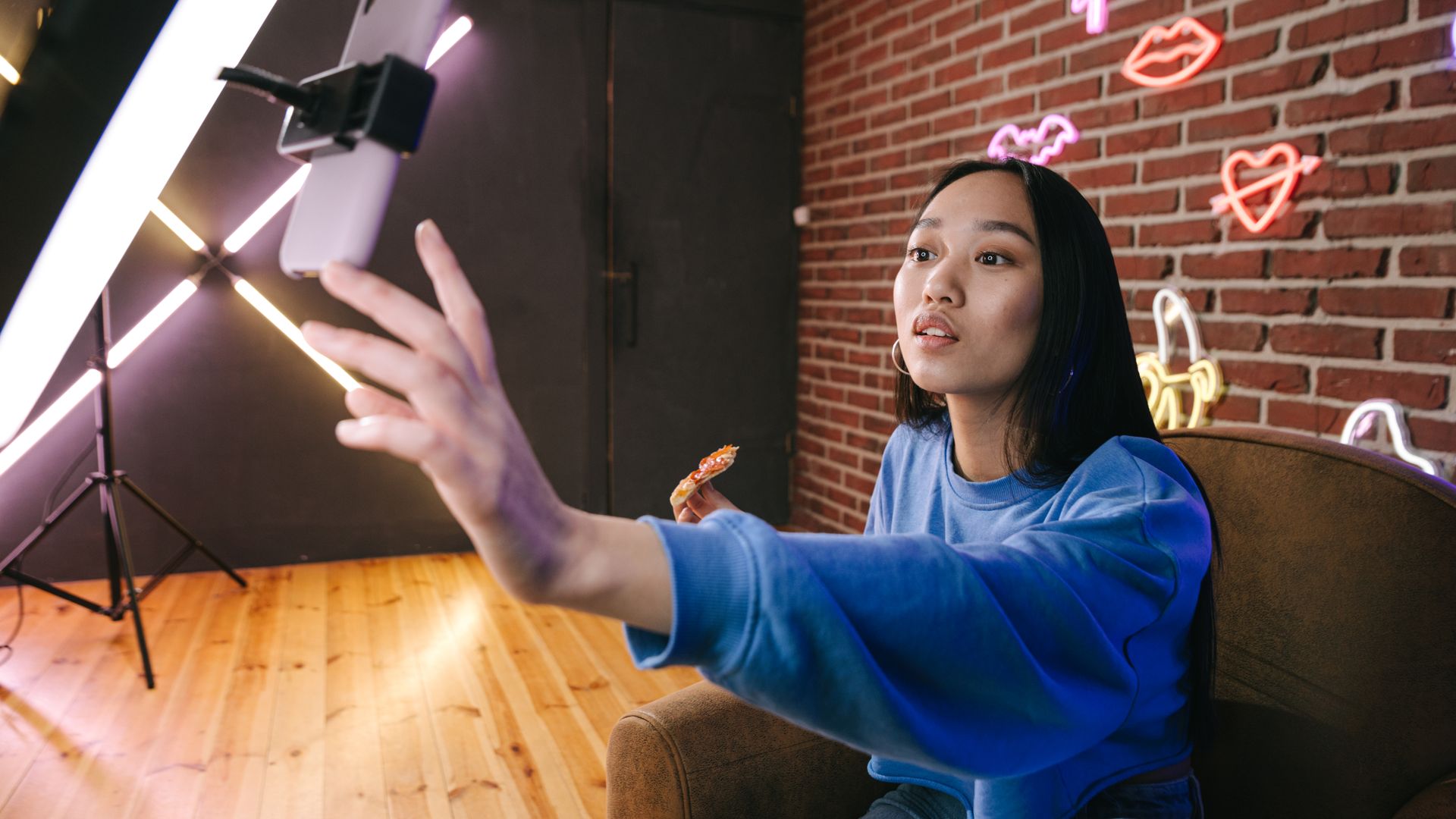 Creatorin am Smartphone im neonbeleuchteten Studio (Symbolfoto)