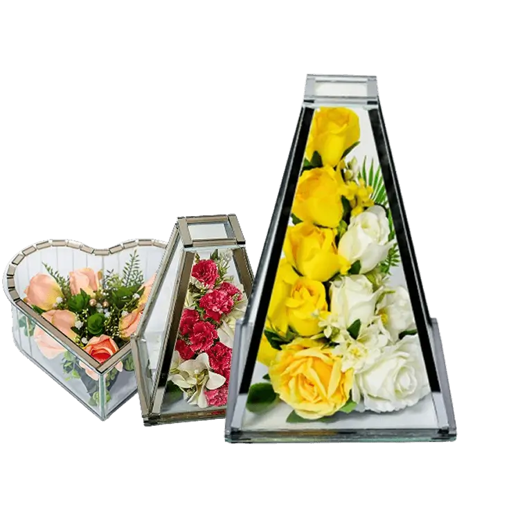 Three glass terrariums containing mixed flower arrangements including white and pink roses, green foliage, red berries, and a pine cone.