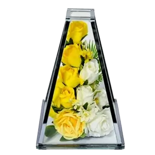 Clear glass pyramid vase containing yellow and white roses with green leaves inside.