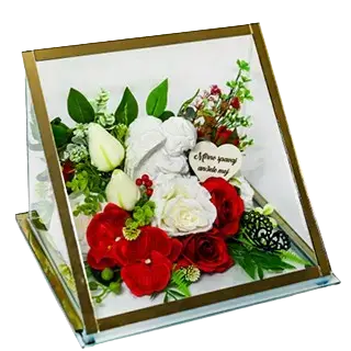 Memorial plaque with an angel figure surrounded by red and white flowers and green leaves inside a transparent case.
