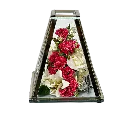 Triangular glass lantern with a metal frame containing red and white artificial flowers inside.