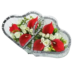 Heart-shaped arrangement of red calla lilies and small white flowers with green leaves framed in a mosaic-edged vase.