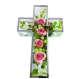 Glass cross filled with pink roses and green foliage on a white background.