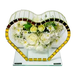 Heart-shaped mirror with yellow mosaic border reflecting a bouquet of white and yellow flowers.