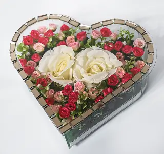 Heart-shaped glass container holding white roses and red calla lilies with green foliage.