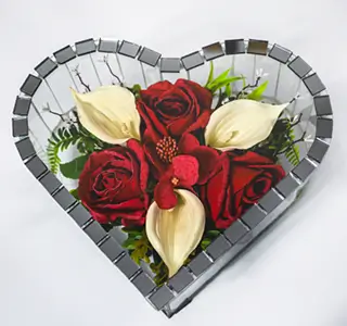 Rectangular glass and gold-trimmed display box containing an arrangement of white, cream, and peach artificial flowers with green foliage and a decorative silver butterfly.
