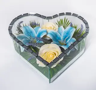 Heart-shaped mirrored tray holding an arrangement of orange and yellow flowers with green foliage and a decorative yellow butterfly.