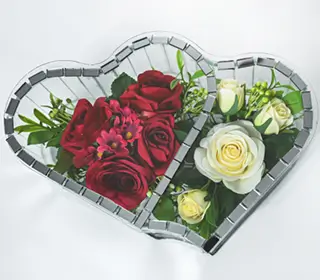 Two heart-shaped glass containers holding red and white roses with greenery inside.