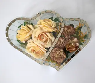 Heart-shaped glass container holding peach roses, white calla lilies, small yellow flowers, and a decorative butterfly.