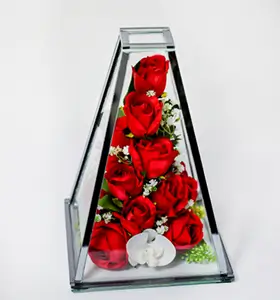 Triangular glass vase containing white calla lilies, blue and white roses, and green foliage on a white background.