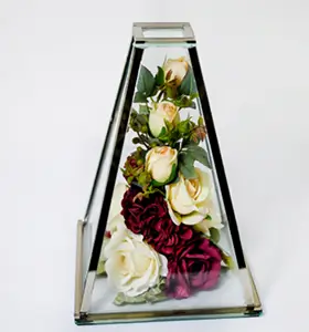 Triangular glass display case containing white and dark red roses with green leaves inside.